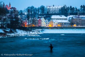 Ein Angler steht im eiskalten Lech vor dem Lechwehr und der Altstadt von Landsberg